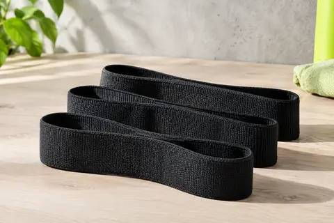 Trois mini-bandes de résistance en tissu noir posées sur une surface en bois clair