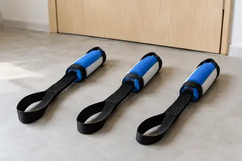 Trois ancrages de porte posés au sol, chacun formé d’une sangle plate en nylon noir cousue et d’une butée en mousse bleue et blanche.