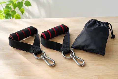 Deux poignées en mousse noire à liserés rouges, avec sangles et mousquetons en acier, posées séparément près d’un petit sac noir.