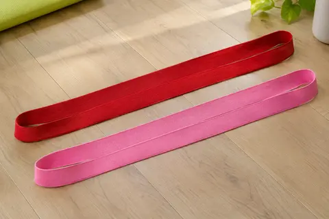 Deux longues bandes de résistance en tissu, rouge et rose, étendues côte à côte sur un parquet clair.