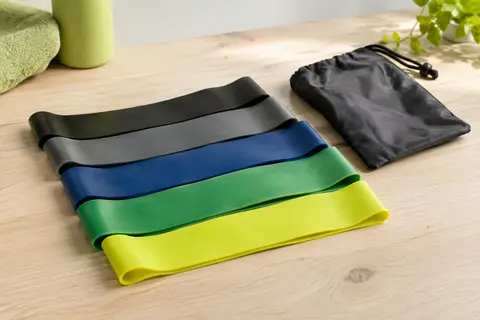 Cinq mini-bandes de résistance multicolores en boucle posées sur une surface claire avec leur sac de transport