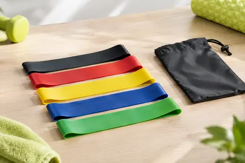 Cinq mini-bandes élastiques multicolores en latex naturel posées sur une surface claire avec leur sac de transport