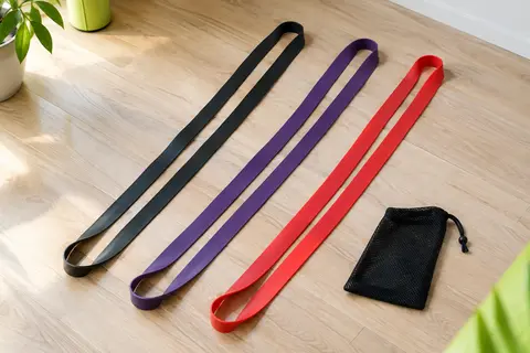 Trois longues bandes élastiques en boucle, noire, violette et rouge, étendues côte à côte près de leur sac en maille.