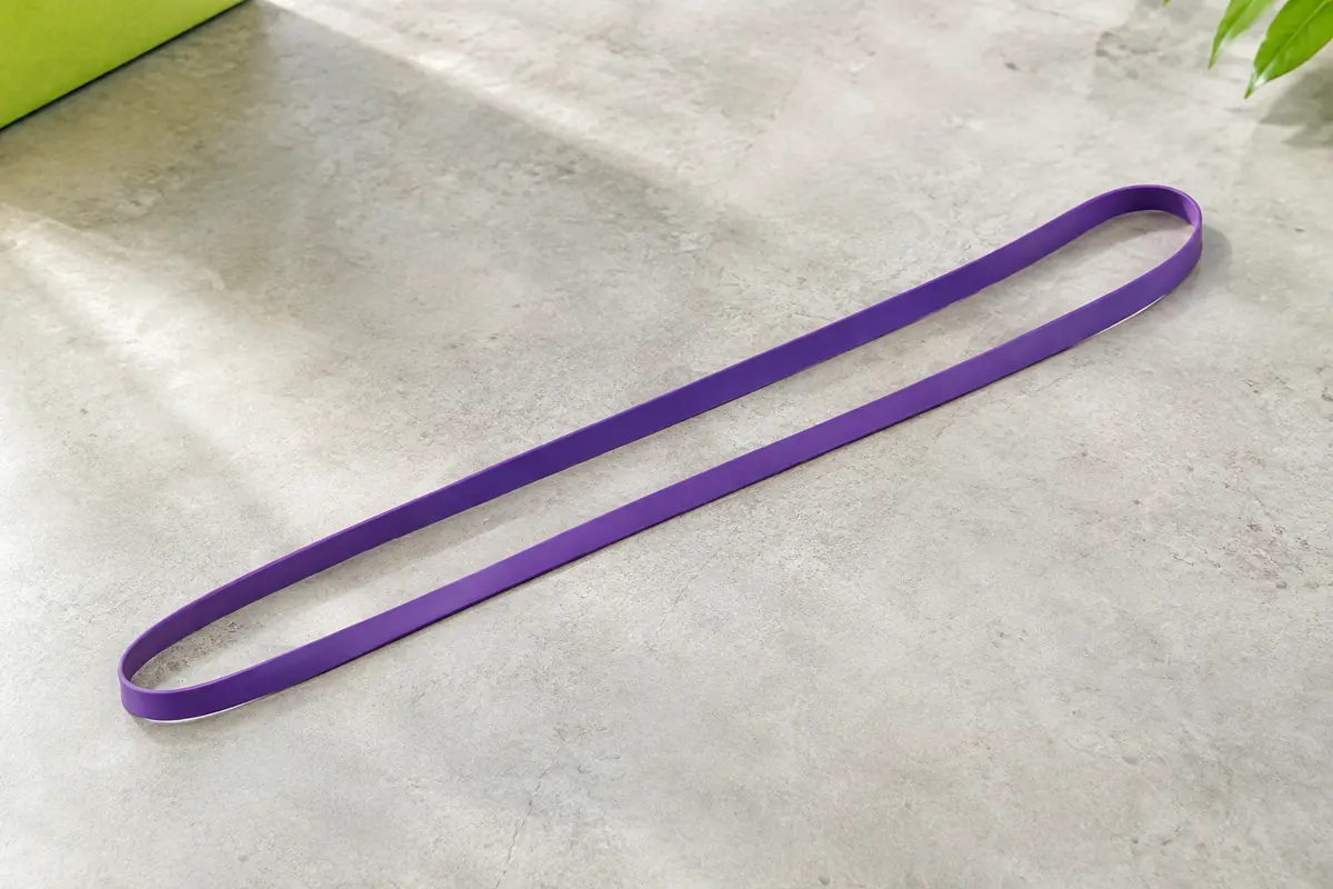 Longue bande élastique violette en boucle, fine et étendue sur toute sa longueur sur un sol clair.