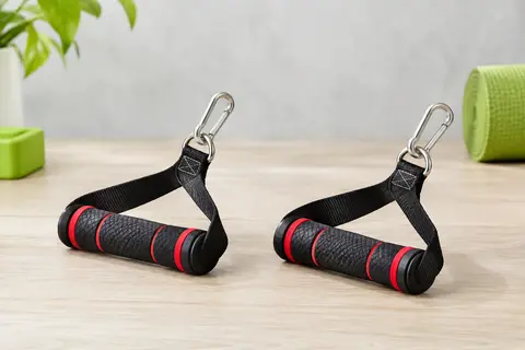 Paire de poignées en caoutchouc noir à accents rouges, avec sangles cousues et mousquetons métalliques, posées sur un bois clair.