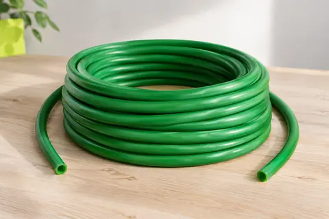 Bobine de tube élastique vert en latex enroulée en nombreuses spires, aux extrémités libres, posée sur un bois clair.