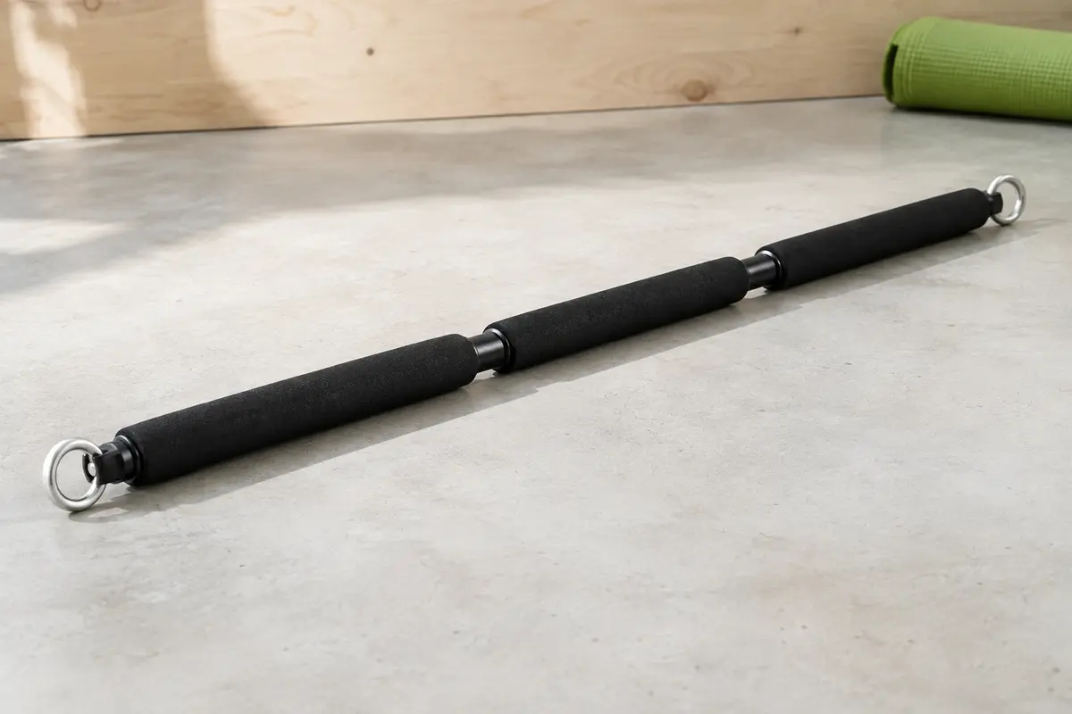 Barre de résistance noire assemblée, en trois sections gainées de mousse, avec un anneau pivotant à chaque extrémité, posée sur un sol en béton clair.